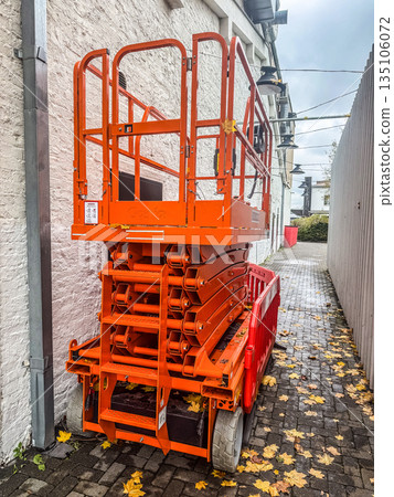 Orange Electric Scissor Lift in an Alley 135106072