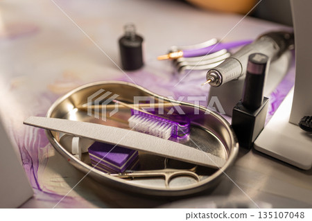 Professional manicure tools set on nail technician workspace. Nail file, scissors, brushes, electric drill and cosmetics arranged on table in beauty salon. Nail care equipment and hygiene concept. 135107048