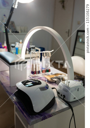 Modern manicure workspace in beauty salon with professional table, lamps, tools and cosmetics. Nail technician workstation setup, nail care service and beauty industry interior concept. 135108279