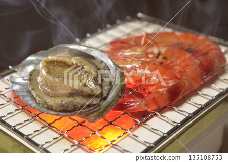 Grilling abalone and shrimp on a smoky charcoal grill 135108753
