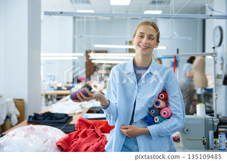 Woman organizing thread spools carefully, brightly colored yarns in industrial sewing environment Woman organizing thread spools carefully, brightly colored yarns in industrial sewing environment 135109485