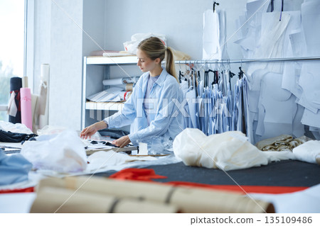 Professional clothing woman creator arranging pattern pieces meticulously during daylight in studio Professional clothing woman creator arranging pattern pieces meticulously during daylight in studio 135109486