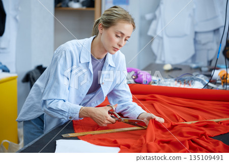 Dedicated seamstress carefully trims and assesses fabric pattern on spacious worktable 135109491