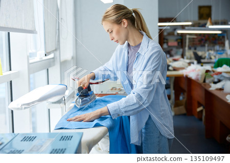 Craftswoman skillfully presses fabric, clothing artisan expertly ironing fabric 135109497