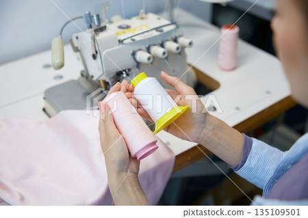Worker organizes colored threads for garment assembly process 135109501