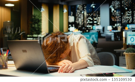 General manager in a dark office at midnight struggles to stay awake after an intense workload, dealing with anxiety due to work tension and fatigue. Mental haze and workplace challenges. Camera A. 135109530