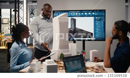 Urban development diverse team discussing property investment new strategy for project approval in a bright office setting, analyzing blueprints and 3D models on architectural software. 135109538