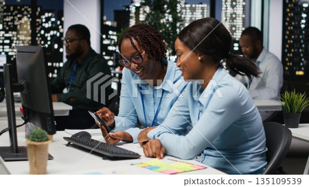 Black business people working together on report writing in dark office, collaborating on building a new development strategy after hours. Reviewing insights to enhance efficiency. 135109539