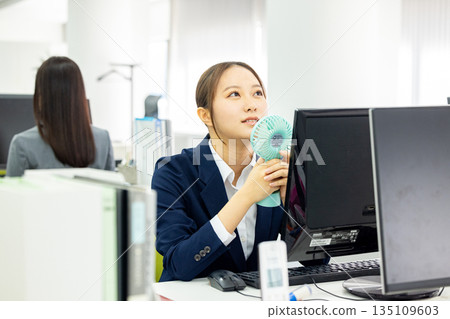 Young woman using an electric fan in the office 135109603