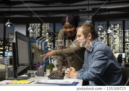 Diverse engineering team designing a floor plan on dual monitors, using computer for interior design customization and rendering. Young man uses digital rendering and remodeling. 135109725
