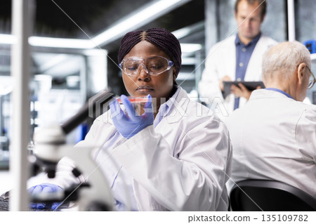 Black chemist examining Petri dish in modern laboratory with a pathology investigation, molecular analysis and biochemistry research. Innovation in diagnostics and biotechnology. 135109782