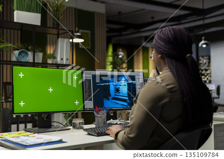 African american woman works on game developing with green screen, using dual monitors at the office. Female engineer creating a futuristic spaceship station on modern software. African american woman works on game developing with green screen, using dual monitors at the office. Female engineer creating a futuristic spaceship station on modern software. 135109784