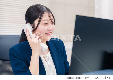 Female business person talking on a landline phone in the office Female business person talking on a landline phone in the office 135110163