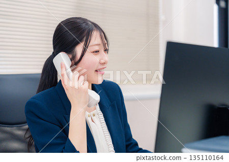 Female business person talking on a landline phone in the office Female business person talking on a landline phone in the office 135110164
