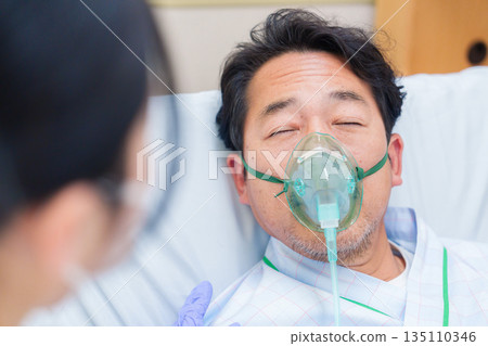 A male hospitalized patient talking while wearing a ventilator 135110346
