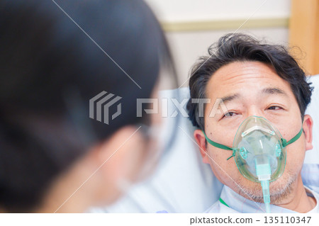 一名男性住院病人戴著呼吸器說話 一名男性住院病人戴著呼吸器說話 135110347