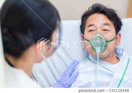 A male hospitalized patient talking while wearing a ventilator 135110349