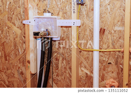 Workers connect plumbing system in new home, laundry room on pipes, fixture installation near framing. Workers connect plumbing system in new home, laundry room on pipes, fixture installation near framing. 135111052