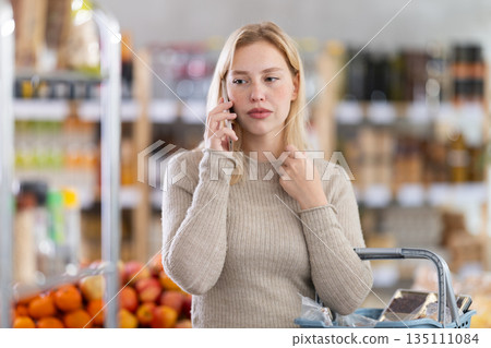 Upset girl talking on smartphone while shopping in supermarket 135111084