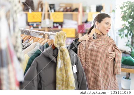 Selective middle-aged woman choosing winter dress in clothing store Selective middle-aged woman choosing winter dress in clothing store 135111089