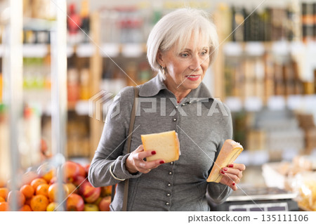 Elderly woman choosing cheese in grocery store Elderly woman choosing cheese in grocery store 135111106