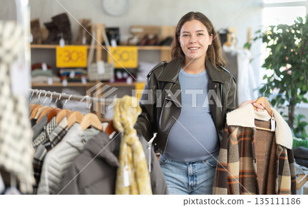 Pregnant woman chooses checkered jacket searches for fashionable clothes in clothing boutique 135111186