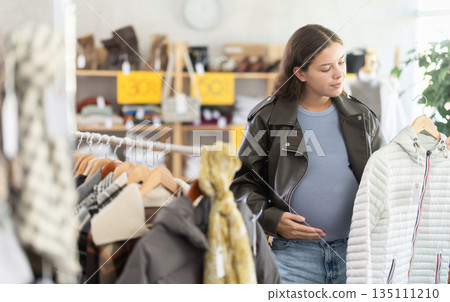 Pregnant woman choosing down jacket in clothing store 135111210