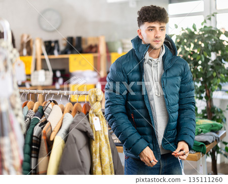 Young man trying on down jacket in clothing store 135111260