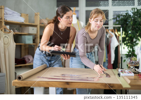 Young designers sketching garment pattern and using tablet in studio 135111345