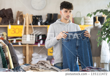 Regular customer guy chooses color and style of jeans trousers Regular customer guy chooses color and style of jeans trousers 135111472