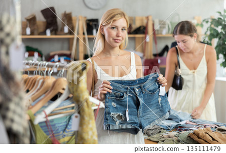 Woman holds shorts in her hands against the background of a customer in a store Woman holds shorts in her hands against the background of a customer in a store 135111479