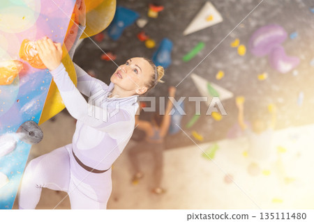 Adult woman practicing rock climbing on climbing wall 135111480