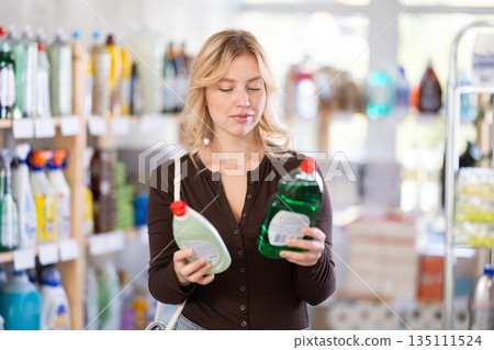 Focused young Woman choosing dishwashing liquid on supermarket shelf 135111524