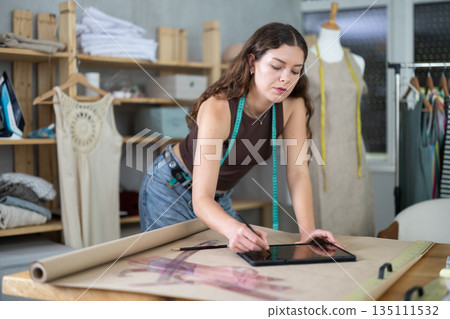 Tailor drawing fashion design on tablet in workshop 135111532