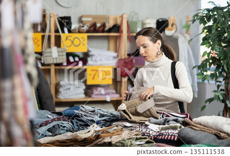 Selective middle-aged woman choosing trousers in clothing store 135111538