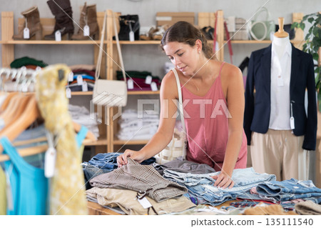 Young woman choosing pants on a shelf in a store Young woman choosing pants on a shelf in a store 135111540