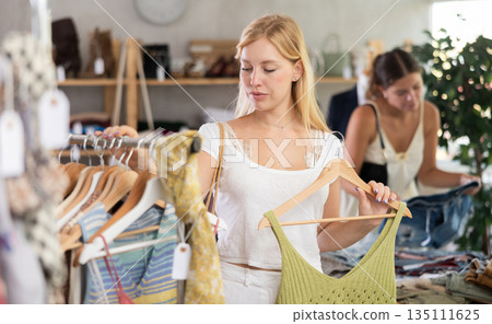 Girl buying something clothing for summer. Female client looking for something in background Girl buying something clothing for summer. Female client looking for something in background 135111625