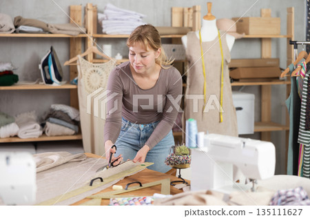 Tailor woman cutting fabric in the workshop Tailor woman cutting fabric in the workshop 135111627
