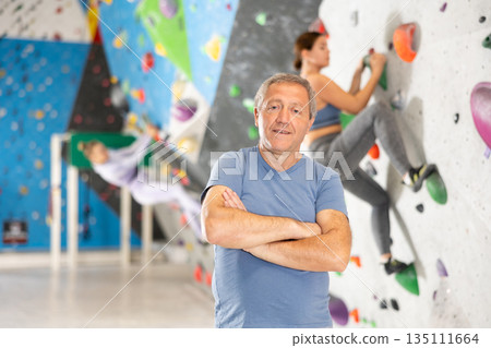 Positive experienced elderly climber standing near bouldering wall Positive experienced elderly climber standing near bouldering wall 135111664