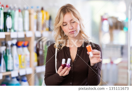 Smiling young woman customer deciding on nail polish in beauty department at store Smiling young woman customer deciding on nail polish in beauty department at store 135111673