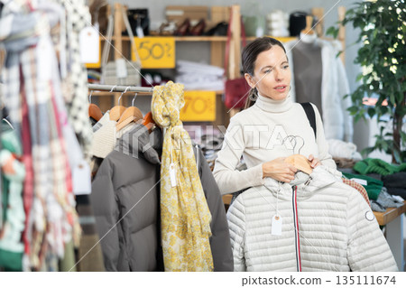 Adult woman chooses outerwear in store Adult woman chooses outerwear in store 135111674