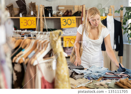 Fashionista girl near showcase examine goods, buying shorts or trousers Fashionista girl near showcase examine goods, buying shorts or trousers 135111705