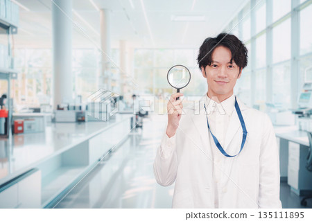 A man in a white coat holding a magnifying glass 135111895