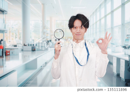 A man in a white coat holding a magnifying glass 135111896