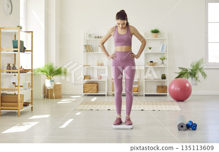 Beautiful fit young woman does sports workouts and weighs herself on scales at home Beautiful fit young woman does sports workouts and weighs herself on scales at home 135113609