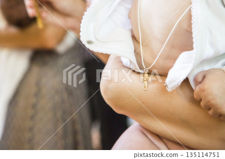 moscow, russia, 18.08.2017 A baby wearing a gold cross necklace is being held by a woman 135114751