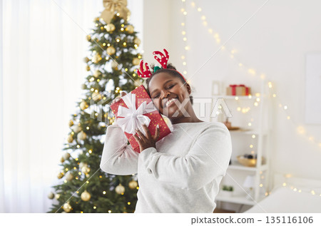 Young happy cheerful girl holding red present gift box celebrating Christmas or New Year Young happy cheerful girl holding red present gift box celebrating Christmas or New Year 135116106