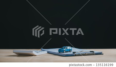 Blue miniature car rests on finance document, outlining terms for auto loan and purchase, calculator stands nearby, representing costs for car contract, lease, sale, or insurance at dealership 135116199
