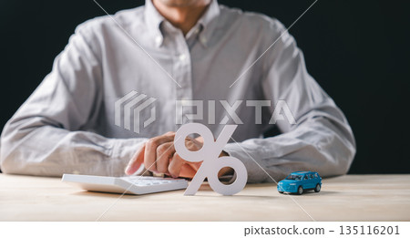 Person working on calculations for car interest rate, pressing buttons on calculator, miniature auto model rests near prominent percent sign representing finance loan options and sale 135116201