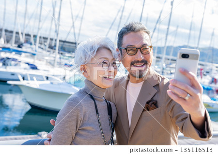 Senior couple taking a selfie at the harbor. Photo courtesy of Ito Marine Town Roadside Station. 135116513